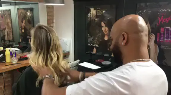 Interior do salão: cliente sendo atendida no espelho, com bancada de madeira e quadros na parede